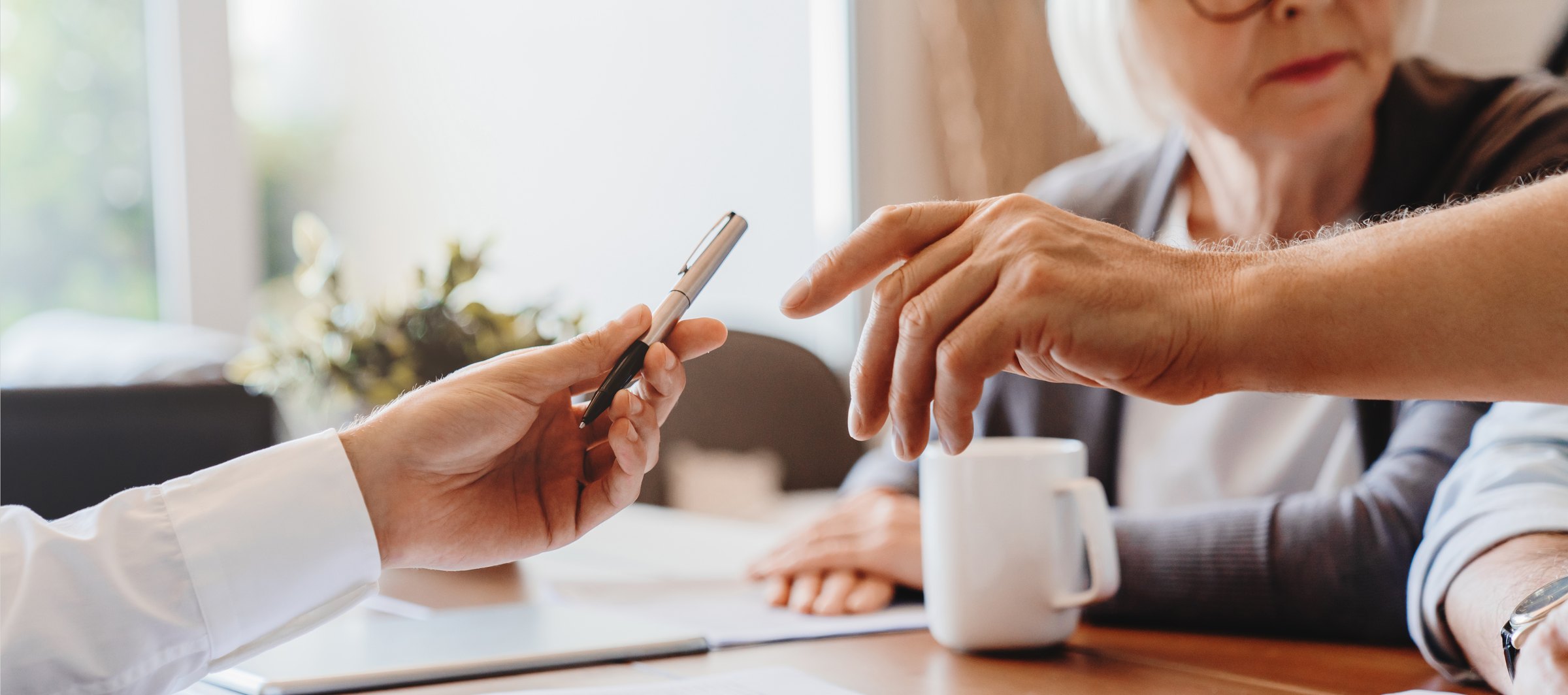 A financial professional passing a pen to an older woman across a table of documents